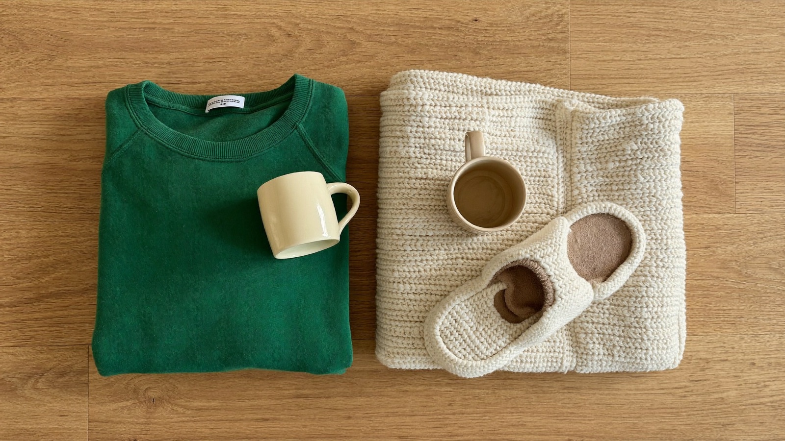 Sudadera verde, cobija, taza y pantuflas sobre una mesa de madera